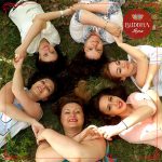 A foto mostra 6 moças, deitadas no chão, com os braços cruzados na frente do corpo, dando a mão umas para as outras. Elas formam um círculo. Isso para mostrar que o trabalho voluntariado traz amor e bem-estar